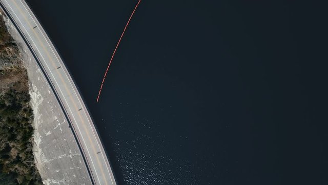 Overhead Drone Shot Over A Road On A Dam In Front Of A River And A Passing Red Car (Hungry Horse Dam, Flathead River, Montana, USA)