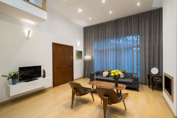 Modern interior of living room in private house. View of wall with big window. Furniture and TV.