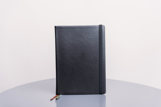 Black Book, Agenda Or Planner Standing On A Grey Surface And White Background. Book Template.