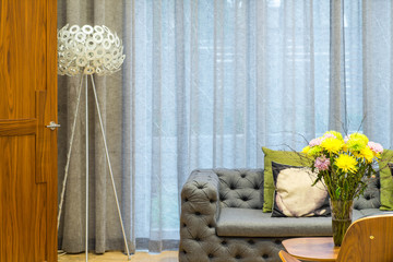 Grey sofa. Vase with flowers on the wooden table. Modern floor lamp. Curtained window. Close-up.