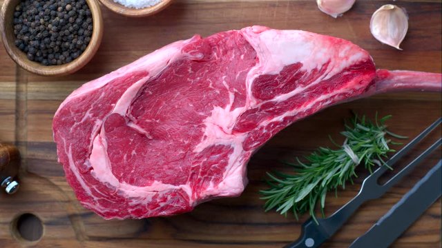 fresh raw tomahawk steak on wooden cutting board