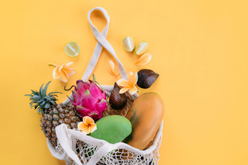 String bag with organic tropical fruits on yellow background. Shopping food with eco friendly bag. Caring for the environment, rejection of plastic, zero waste, recycling concept.