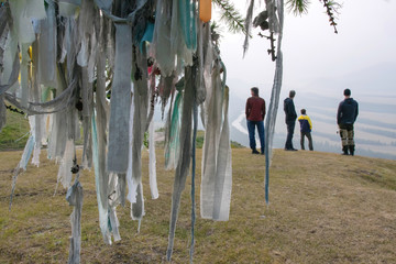 Prayers ribbons (Turkic: djalama or kyra) on the tree on a mountain pass and group of tourists. Argut river region, Altai Republic; Siberia, Russia.