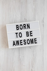 Obraz premium 'Born to be awesome' words on a modern board on a white wooden background, top view. Overhead, from above, flat lay.