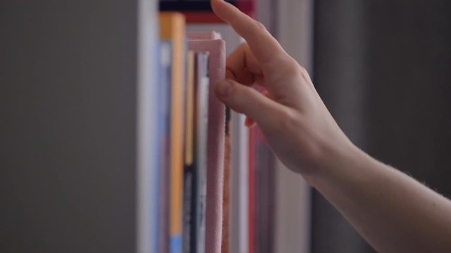 Hand reaches for and pulls classic book from library shelf
