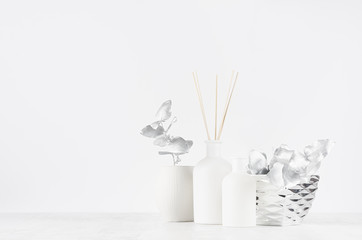Modern exquisite decoration for home interior -  aromatherapy white bottles with sticks, ceramic vase, silver leaves, bowl on white wood background.