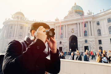 Young Asian man tourist taking photos with camera in hands near Hofburg palace in Vienna, Austria,...