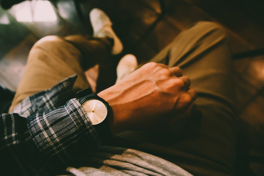 The manin tartan shrit sitting on chair wears a tartan shirt looking at his analog watch on his hand watching the time at the coffee shop. waiting for an appointment.