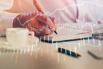 Double exposure of man's hands writing notes of stock market with forex chart.