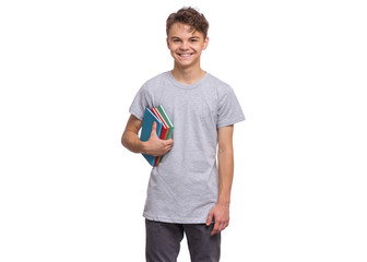 Student teen boy in grey t-shirt holding books and looking at camera. Portrait of cute smiling schoolboy with notebooks, isolated on white background. Happy child Back to school.