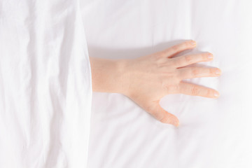Woman's hand is visible from under the covers as a symbol of fight against insomnia. Tired and exhausted person falls asleep only in the morning. Snow-white bedding.