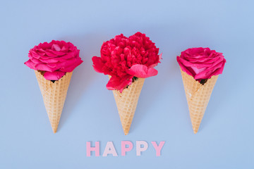 Ice Cream Cones with pink peony and roses on blue background and happy text, flat lay. Valentine's day concept