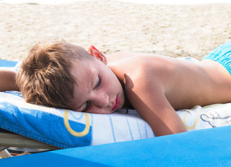 A boy sleeps on the beach under strong sunlight. Danger of sunstroke or burn. The risk of...