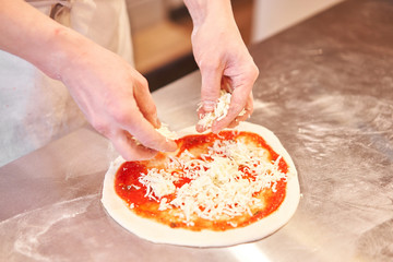 Cooking pizza. arranges cheese ingredients on the dough preform. Closeup hand of chef baker in uniform white apron cook at kitchen