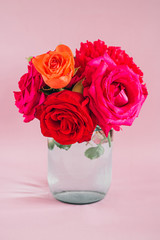 Fototapeta premium Bouquet of red and pink peonies and roses in a glass vase with water on a pink background