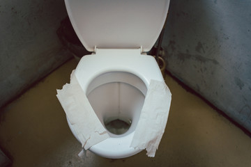 Filthy toilet seat covered with toilet paper as sit down insulation