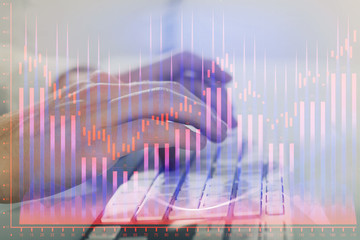 Double exposure of graph with man typing on computer in office on background. Concept of hard work. Closeup.