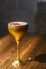 Cocktail with white foam decorated with red dried peppers served in the metal gold glass on the wooden bar table