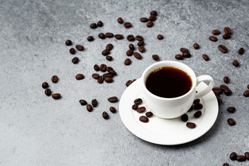 Black coffee in a white cup with roasted coffee beans. Cup of coffee with grains. 