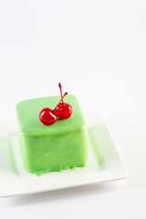 Mousse green cake with cherry dressing on white plate