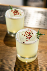 Green lime cocktail with white foam served in rocks glass on the wooden bar table decorated with red dried pepper and rosemary