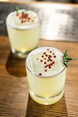 Green lime cocktail with white foam served in rocks glass on the wooden bar table decorated with red dried pepper and rosemary