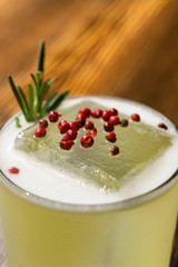 Green lime cocktail with white foam served in rocks glass on the wooden bar table decorated with red dried pepper and rosemary