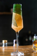 A gold cocktail served in a champagne glass on the wooden bar table and decorated with green bamboo leaf inside