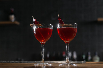 Red cocktail in the wine glass decorated with dried slice of lime and cherry served on the wooden bar desk