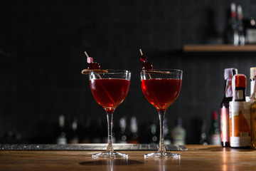 Red cocktail in the wine glass decorated with dried slice of lime and cherry served on the wooden bar desk