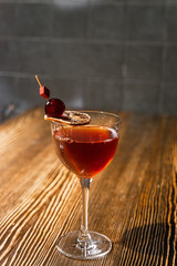 Red cocktail in the wine glass decorated with dried slice of lime and cherry served on the wooden bar desk