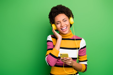 Photo of beautiful dark skin lady hold telephone modern technology earphones listen new popular songs eyes closed wear casual striped jumper isolated green color background