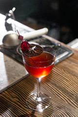 Red cocktail in the wine glass decorated with dried slice of lime and cherry served on the wooden bar desk