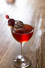 Red cocktail in the wine glass decorated with dried slice of lime and cherry served on the wooden bar desk