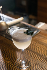 White matte cocktail in the wine glass with foam served on the wooden bar table decorated with green leaf on the top 