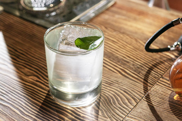 Transparent cocktail in rocks glass decorated with one big ice cube and green leaf served on the...