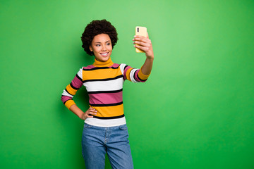 Photo of beautiful dark skin curly lady holding telephone hands making selfies for popular online website blog wear casual striped pullover jeans isolated green color background