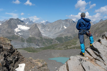 A mountain climber looking at gorgeous alpine landscape with green lake in hanging valley.