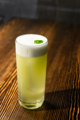 Green cocktail on bar counter. Drink with martini, gin, rum, tequila with alcohol and white foam on...