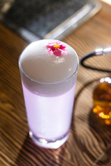 Space violet alcoholic drink in the big cocktail glass decorated with a red flower on the wooden bar desk counter under the studio lights