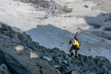 A mountain climber climb down the mountain pass on the background of glacier..