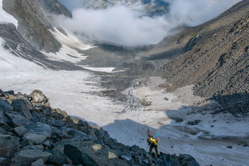 A mountain climber climb down the mountain pass on the background of glacier..
