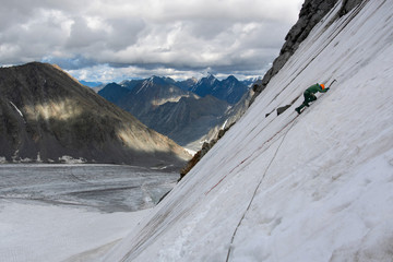 A mountain climber climbs on a steep icy slope on the background of alpine landscape.