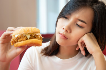 hungry worried woman on diet looking and hesitating to eat fried chicken burger sandwich; concept...