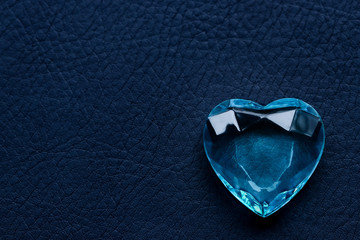 Blue glass faceted heart on a blue leather background horizontal