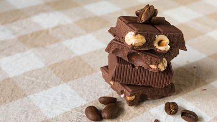 pieces of chocolate with hazelnuts and coffee beans on a brown tablecloth
