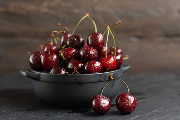 Fresh sweet cherries with water drops in bowl on dark rock table.