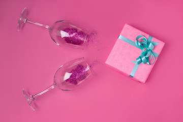 Obraz na płótnie Canvas Pink gift with a turquoise ribbon on a pink background next to the glasses filled with sparkles. The concept of the holidays Valentine's Day, Women's Day, Birthday