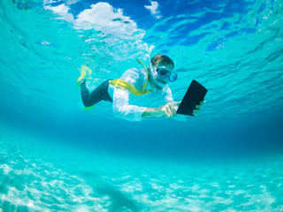 Snorkelling businessman in shirt and tie and matching fins using a tablet computer while swimming...