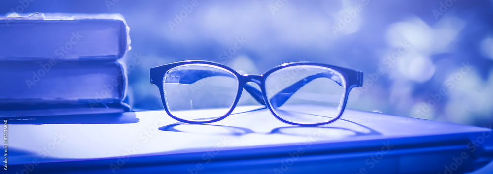 Poster stack of books with glasses placed on the open book in library.